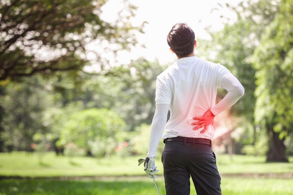 Man playing golf, holding his back in pain