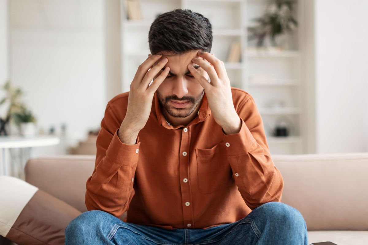 Man sitting on couch with his head in his hands, experiencing a headache