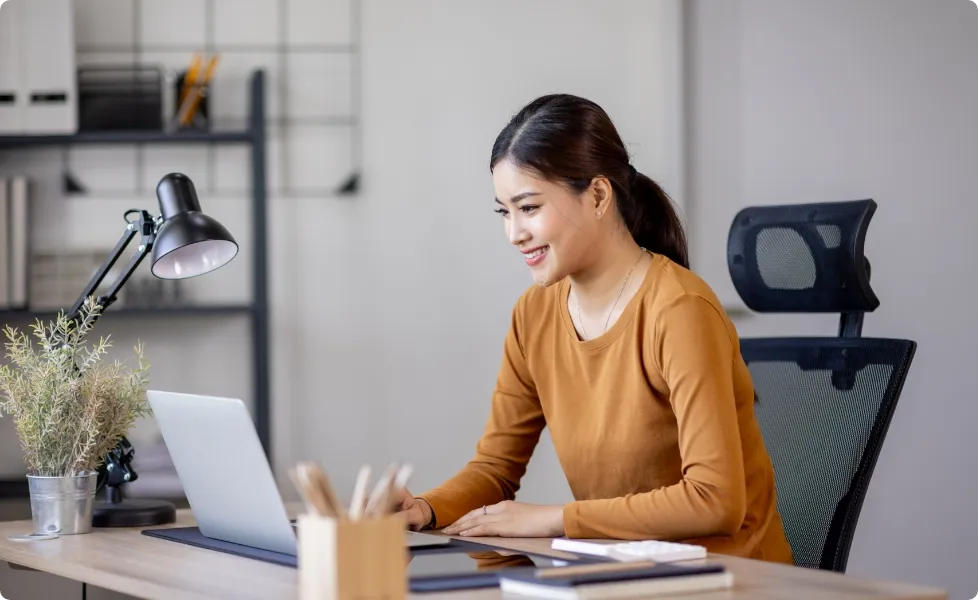 A young woman smiling while working on a laptop at a desk.