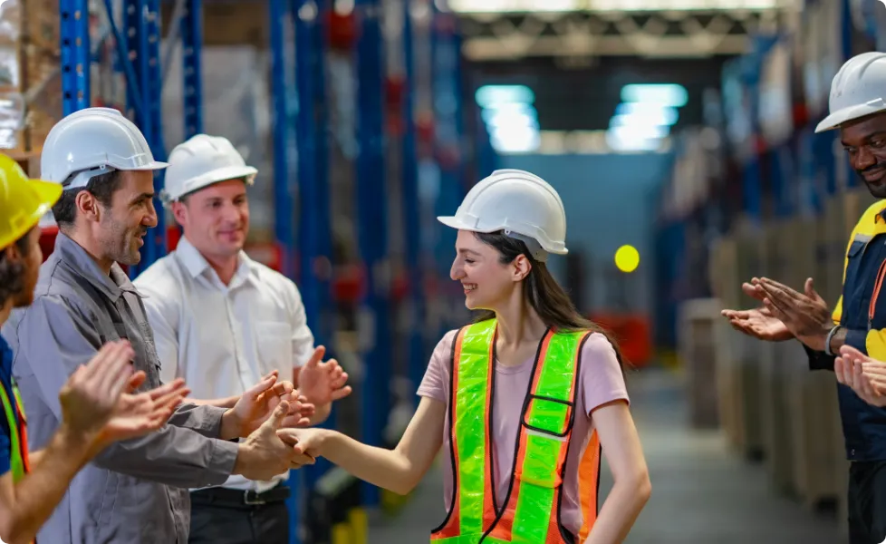Warehouse workers applauding a colleague during a handshake in a distribution center.