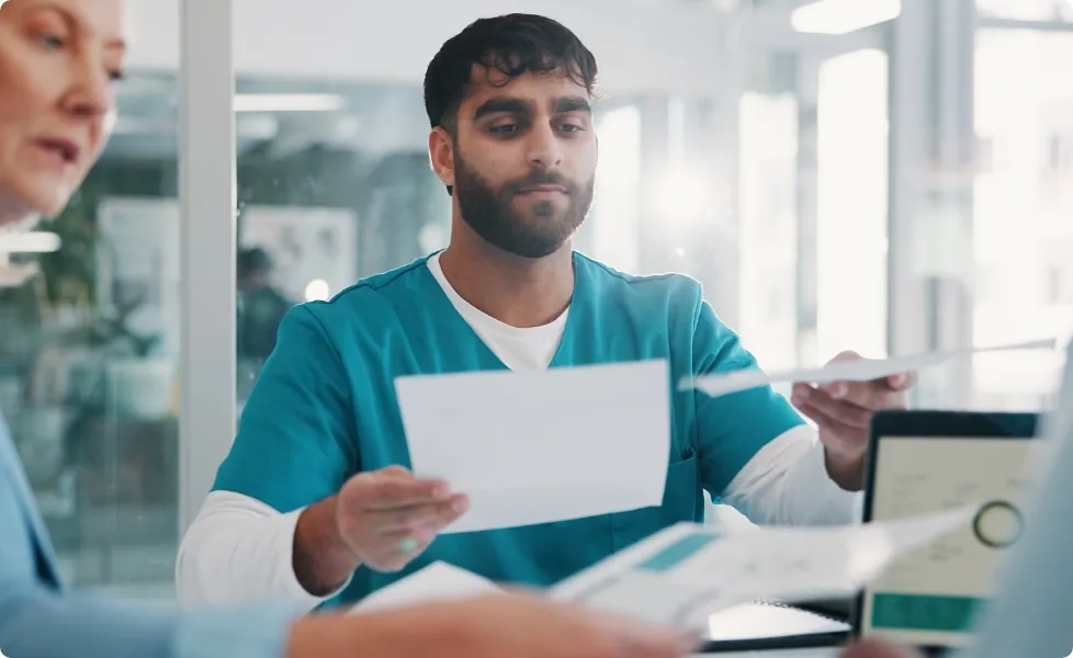 A healthcare worker in teal scrubs handling documents at a clinic desk.