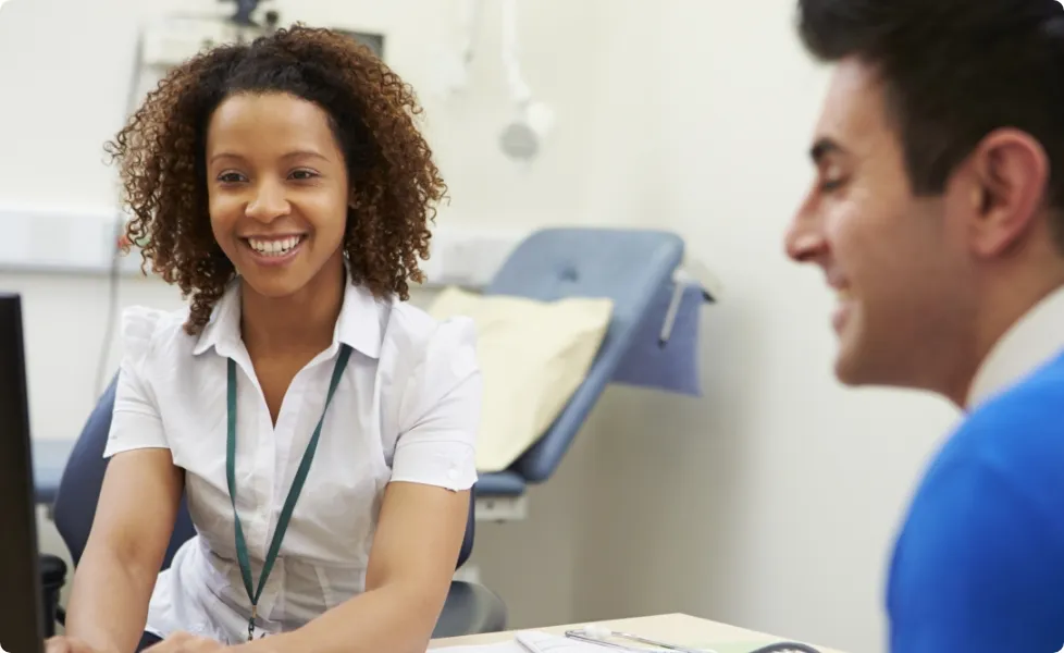 A healthcare worker smiling while speaking with a patient at a desk.